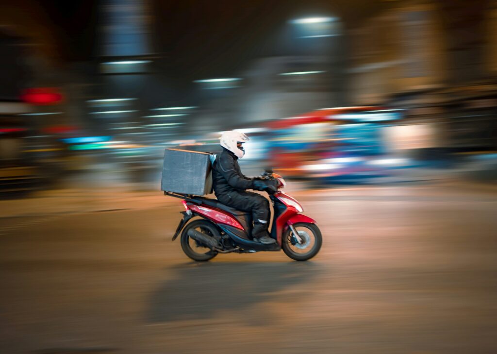 Un scooter rouge dans la nuit, conduit par un livreur qui porte un casque.