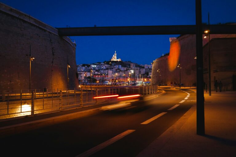 une rue de circulation de Marseille la nuit avec un pont et en fond la cathédrale Notre-Dame de la Garde sur les hauteurs de la ville.